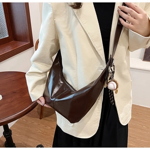 Detail of dark brown glossy hobo bag with baseball charm on shoulder strap