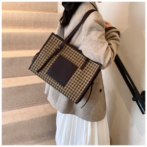Detail of houndstooth tote bag showing leather handles and textured fabric on shoulder
