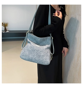 Detail of light blue textured leather crossbody bag with gold hardware on a model