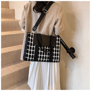 Detailed view of black and white checkered tote bag worn with a casual blazer on a model