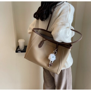Detail view of khaki tote bag with plush monster charm worn by model for daily commute