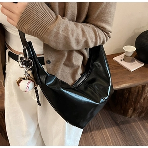 Close-up of a black glossy crescent bag with silver zipper and a baseball pendant detail