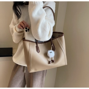 Detail of a large color-block tote bag with a plush monster charm and smooth PU leather texture