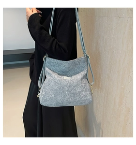 Close-up of light blue textured shoulder bag with golden metal hooks and brand logo detail