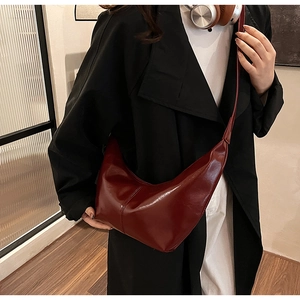 Detail view of a burgundy leather crescent crossbody bag shown with a chic black trench coat