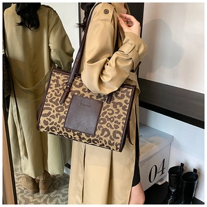 Detail of leopard print tote bag with brown leather handles worn with khaki trench coat
