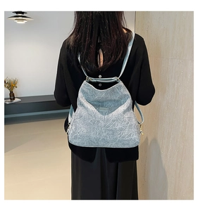 Detail of the light blue textured backpack with gold hardware worn by a model