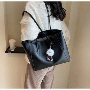 Large black leather tote bag with plush charm shown from the back on a model