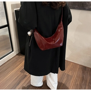 Detail of burgundy crescent bag in glossy finish with unique baseball charm on shoulder strap