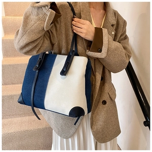 Close-up of contrast large denim tote bag featuring navy leather handles and reinforced base