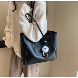 Detailed view of black tote bag featuring contrast stitching and cute plush doll pendant