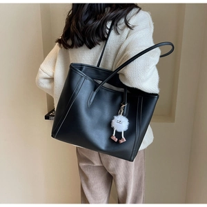Detail of black faux leather tote bag with white plush charm pendant on shoulder