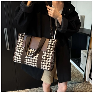 Detail view of large houndstooth tote bag featuring premium brown leather and logo flap