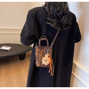Détail du mini sac seau léopard avec une breloque en peluche orange et bandoulière amovible