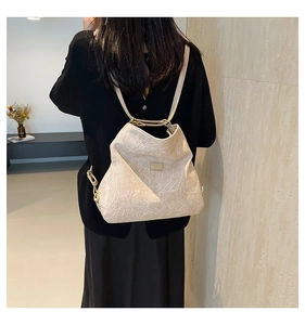 Detail of beige textured backpack with metallic logo plate worn by model from behind