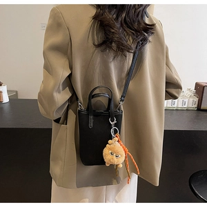 Détail du sac seau noir en daim avec bandoulière et pendentif monstre sur un mannequin