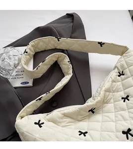Detail of quilted beige shoulder bag with black embroidered bows on grey blazer