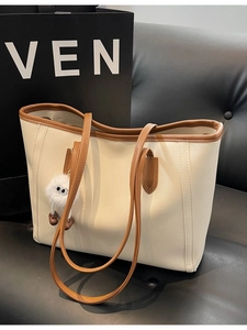 Minimalist beige leather tote bag with brown straps and a cute plush monster charm