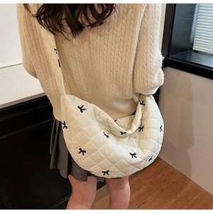 Detail view of cream quilted crossbody crescent bag with tiny black bows on a model