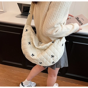 Close-up of quilted cream puffy bag with delicate black bow embroidery detail