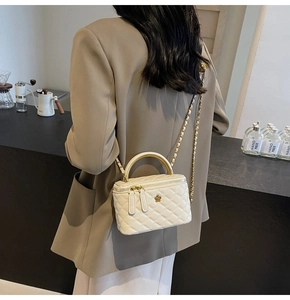 Detail einer gesteppten beigen Box-Tasche mit Goldkette und Blumenverschluss