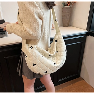 Side view of cream quilted hobo bag with black bow embroidery and puffy strap