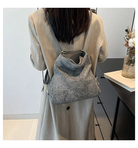 Detailed view of grey textured crossbody bag featuring stylish pleated pattern and gold metal hooks