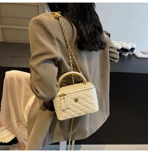 Nahaufnahme der cremefarbenen Stepptasche mit goldener Kamelie und Kettenriemen