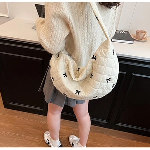 Close-up of quilted cream crescent bag with black bow embroidery worn by a model