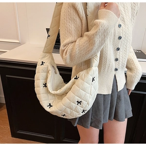 Detail of white quilted crescent bag with black bow accents and light nylon texture