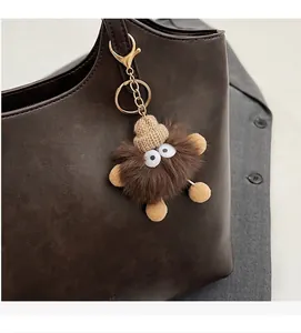 Furry monster bag charm with knit hat and golden clasp on a brown leather tote bag