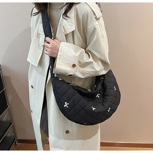 Detail of black quilted crescent bag with white bow embroidery and padded strap