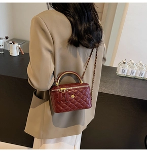 Detail der burgunderroten Stepptasche mit goldenem Metallgriff und Kettenriemen
