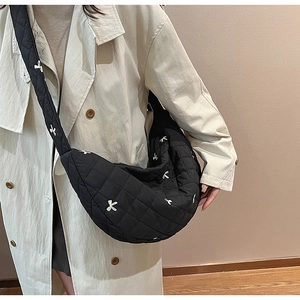 Detail of black quilted crossbody bag featuring delicate white bow embroidery and padded strap