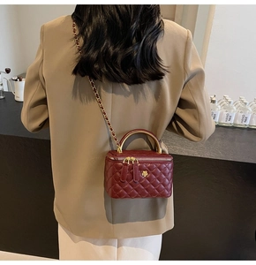 Nahaufnahme der weinroten Stepptasche mit goldener Kamelienblüte und Kettengurt