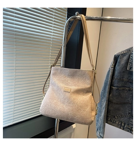 Detail of beige textured shoulder bag with golden logo plate and elegant gold hardware