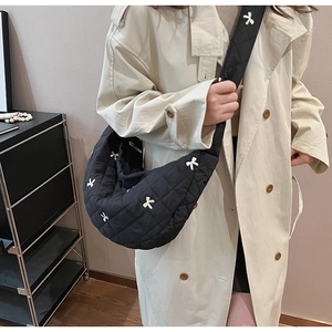 Detailed view of black quilted hobo bag with white bow embroidery on a crossbody strap
