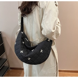Detail view of black quilted dumpling bag with bow embroidery and wide strap
