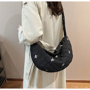 Quilted black crescent bag with mini white bow embroidery worn by model