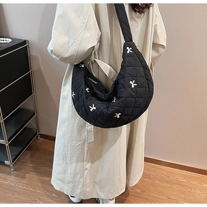 Detail of black quilted half-moon crossbody bag with white bow embroidery on a model