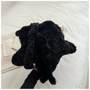 Detail of black plush faux fur tote bag showing soft fuzzy texture on a bed