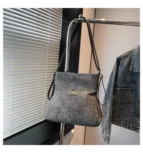 Close-up of gray shoulder bag with stone texture, brand label, and gold hardware