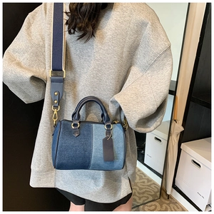 Dettaglio borsa Boston in denim blu con manici in pelle e tracolla larga indossata da modella