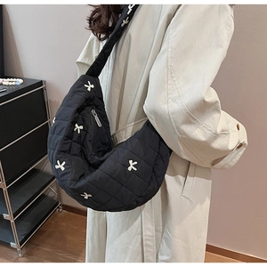 Detail of black quilted crescent crossbody bag with white bow embroidery on shoulder