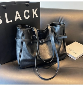 Detail of black faux leather tote bag with silver buckle strap on a dark sofa background