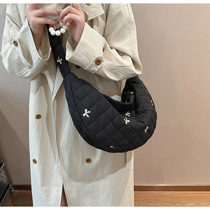 Quilted black crescent crossbody bag with white bow embroidery on long coat model