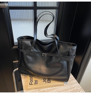 Detail of black leather tote bag featuring a decorative silver buckle strap and soft texture