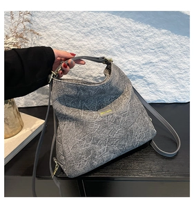 Detail of grey shoulder bag with marble texture and gold hardware on minimalist desk
