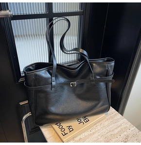 Detailed close-up of a black tote bag showing premium leather texture and silver buckle
