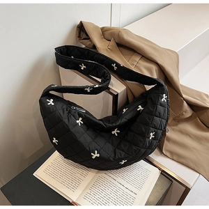 Detail of black quilted crescent bag with small white bows and lattice stitching